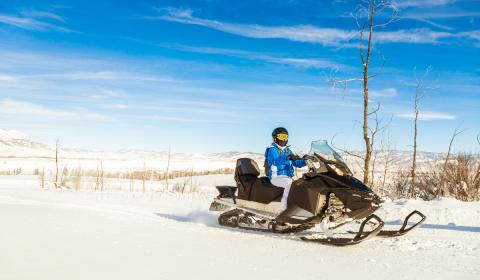Man on snowmobile on hill blue skies