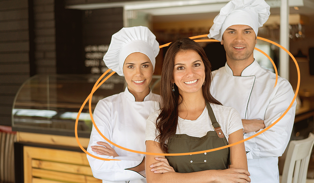 Two female catering servers carrying food out of a kitchen.